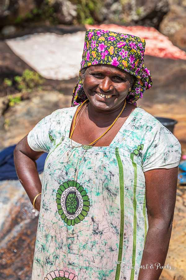 A woman in a floral dress and headscarf smiles at the camera