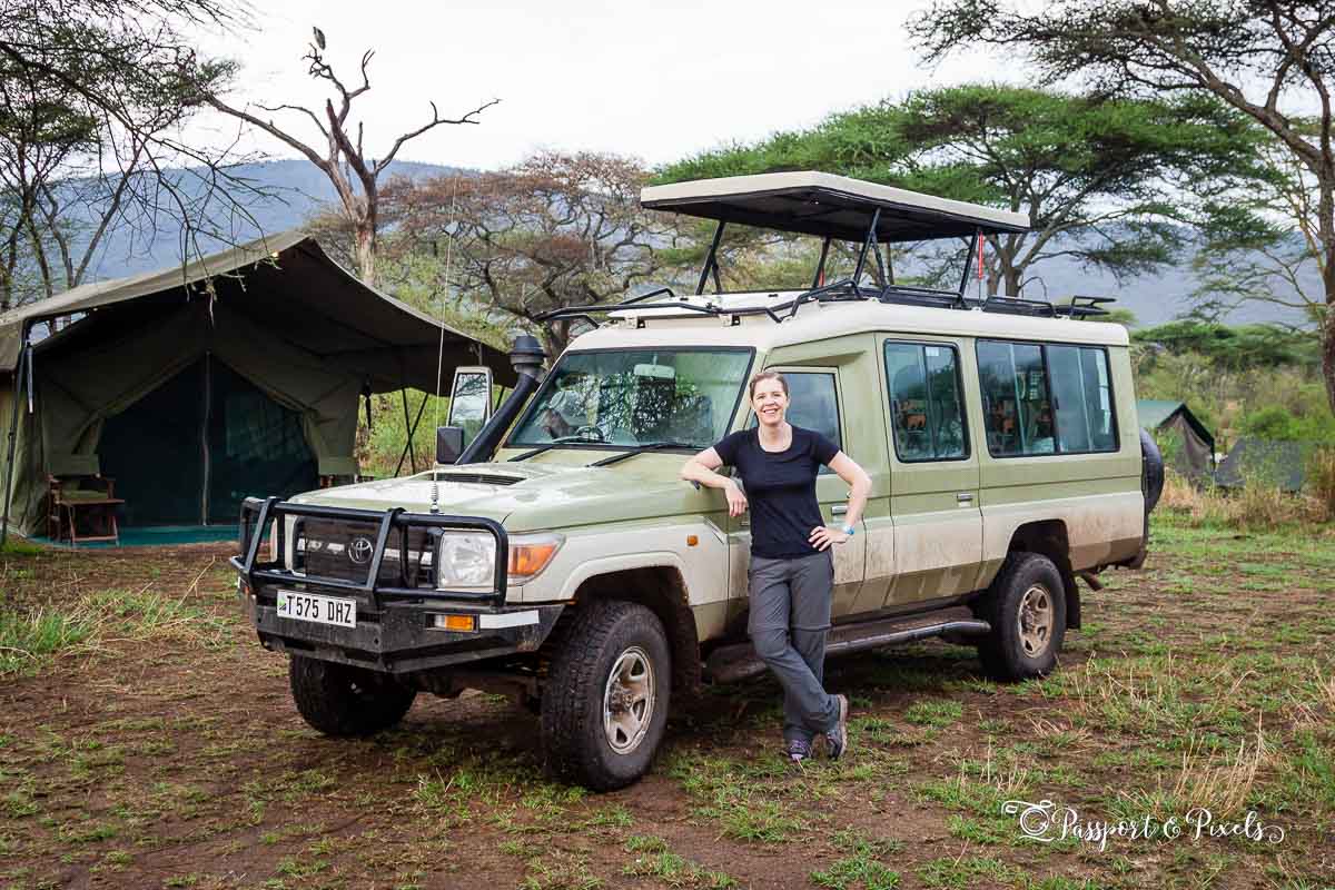 What to pack for safari: the author wearing a black t-shirt and grey zip-off trousers in front of a safari car